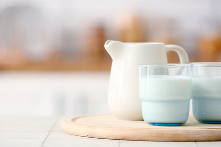 Wooden board with ceramic jug and glasses of milk on white tile tableの写真素材