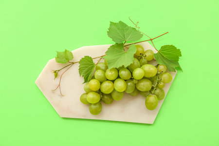 Board with sweet green grapes and leaves on color backgroundの写真素材