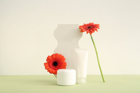 Composition with cosmetic products, plaster podium and beautiful gerbera flowers on color backgroundの写真素材