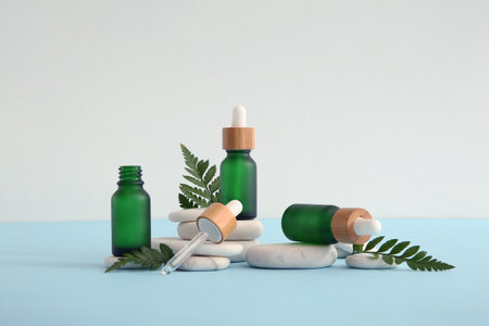 Composition with bottles of essential oil, stones and green leaves on light backgroundの写真素材