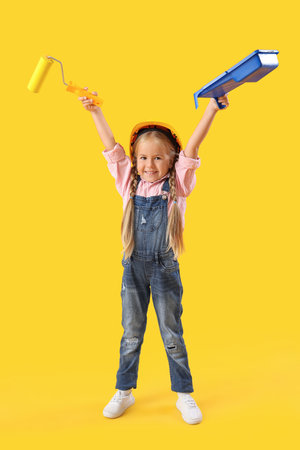 Cute little builder girl with paint roller on yellow backgroundの写真素材