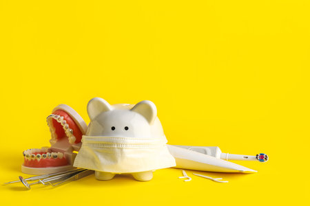 Piggy bank with dental tools and oral care supplies on yellow backgroundの写真素材