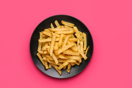 Plate with golden French fries on pink background