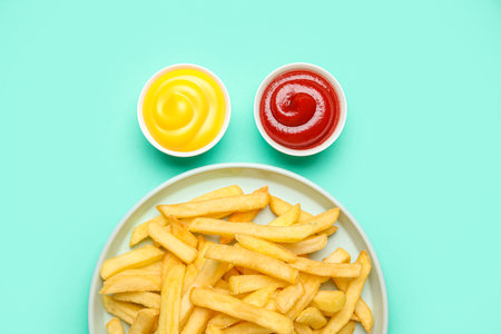 Plate with golden French fries, ketchup and cheese sauce on turquoise backgroundの写真素材