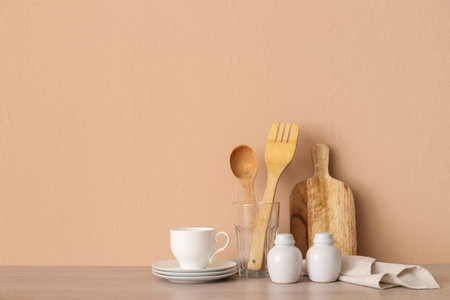 Kitchen utensils, cup and saucers on wooden table near beige wallの写真素材
