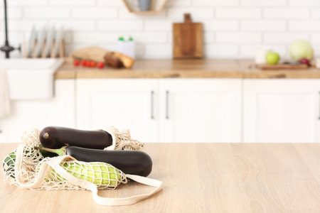 Net with ripe eggplants and zucchinis on table in kitchenの写真素材