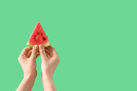 Female hands with slice of ripe watermelon on green backgroundの写真素材