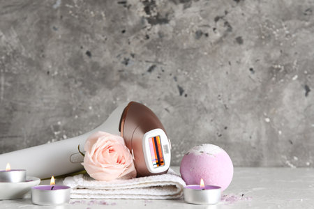 Modern photoepilator with bath supplies, candles and beautiful rose on white table near gray wallの写真素材