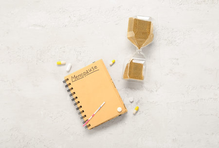 Notebook with word MENOPAUSE, pills, pregnancy test and hourglass on white background