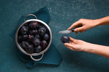 Woman cutting fresh plum on green backgroundの写真素材
