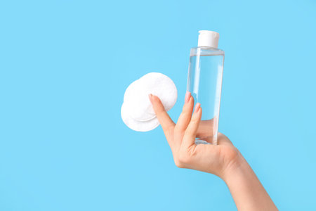 Young woman with micellar water and cotton pads on blue background, closeupの写真素材