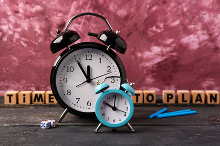 Cubes with text TIME TO PLAN and alarm clocks on wooden table against pink background. Time...
