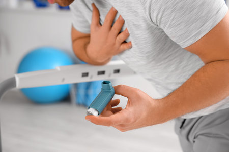 Sporty young man with inhaler having asthma attack in gym, closeup