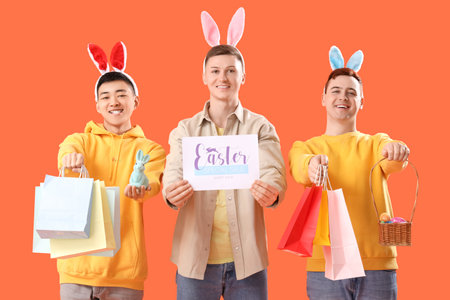 Young man in bunny ears with shopping bags and eggs on orange background. Easter Saleの写真素材