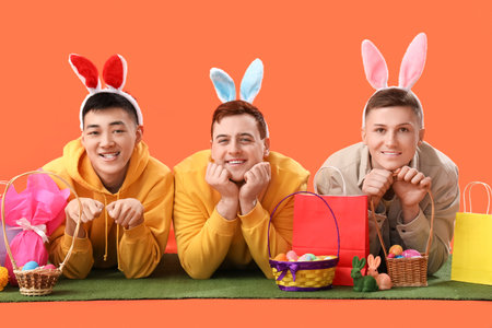 Young men in bunny ears with eggs and shopping bags lying on grass against orange background. Easter Saleの写真素材