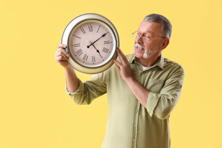 Mature man with clock on yellow backgroundの写真素材