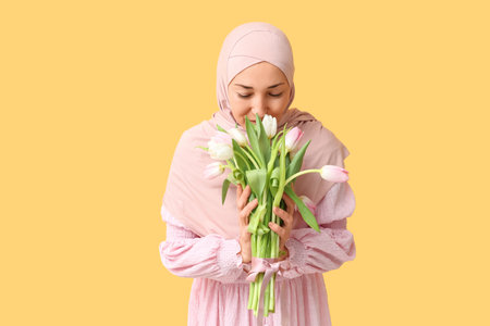 Mature Muslim woman with bouquet of beautiful tulips on yellow background. International Women's Dayの写真素材
