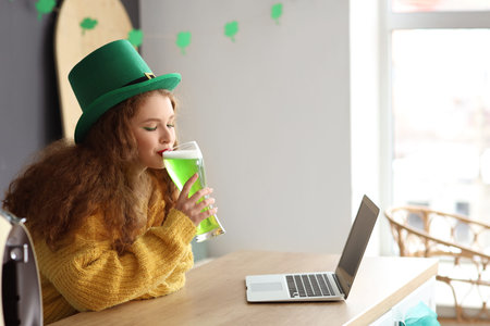 Young woman drinking beer in kitchen on St. Patrick's Dayの写真素材