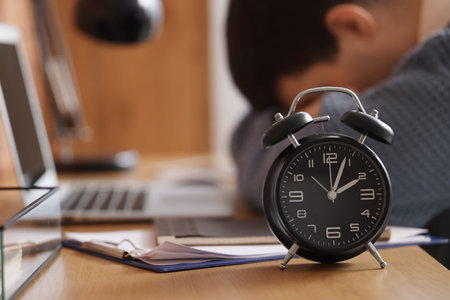 Alarm clock on table of tired businessman in office, closeup