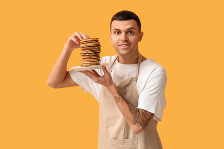 Young man with tasty homemade pancakes on yellow backgroundの写真素材