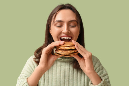 Happy young woman eating tasty pancakes on green backgroundの写真素材