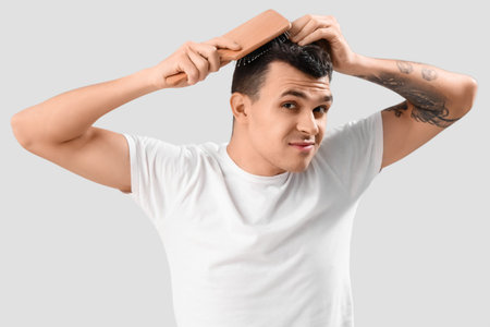 Young man with hair loss problem brushing on light backgroundの写真素材