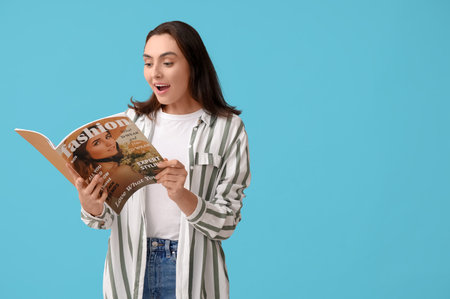 Young woman reading fashion magazine on blue backgroundの写真素材