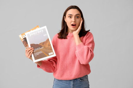 Surprised young woman with magazines on light backgroundの写真素材