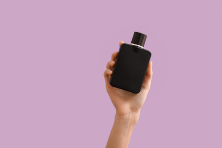 Female hand holding bottle of black perfume on color background, closeupの写真素材