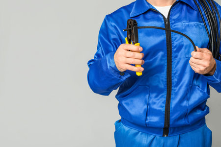 Male electrician with wire and crimper on gray background, closeup