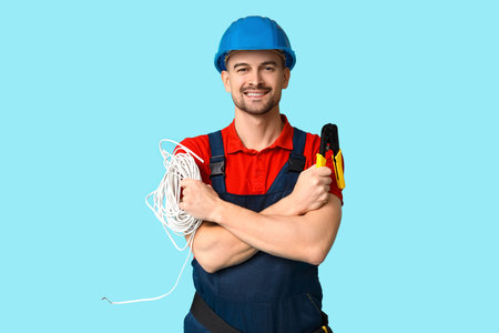 Portrait of male electrician with crimper and wires on blue background