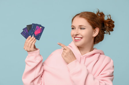 Beautiful young woman pointing at credit cards on blue backgroundの写真素材