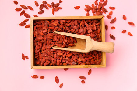 Wooden box and scoop with red dried goji berries on pink backgroundの写真素材