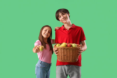Cute girl and her brother with basket full of fresh apples on green backgroundの写真素材