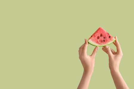 Female hands with slice of ripe watermelon on light green backgroundの写真素材