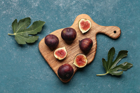 Wooden board with fresh ripe figs and leaves on green background