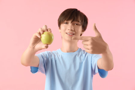 Teenage boy pointing at fresh apple on pink backgroundの写真素材