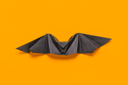 Black origami bat on orange background