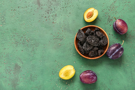 Bowl with tasty dried plums on green backgroundの写真素材