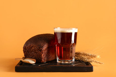 Glass of tasty kvass, bread, yeast and spikelets on orange background