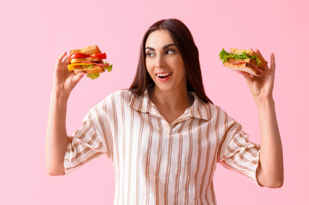 Young woman with tasty sandwiches on pink backgroundの写真素材