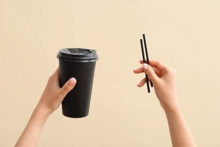 Female hands with black takeaway paper cup and straws on light background