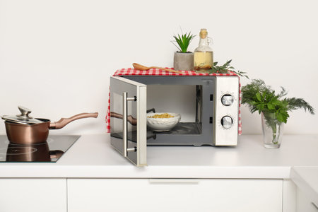 Bowl with pasta in modern microwave oven on white kitchen counter