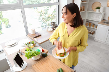 Beautiful young woman with tasty sandwich in kitchenの写真素材