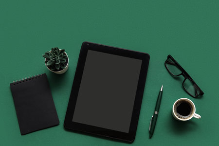 Tablet, cup of coffee and stationery on green backgroundの写真素材