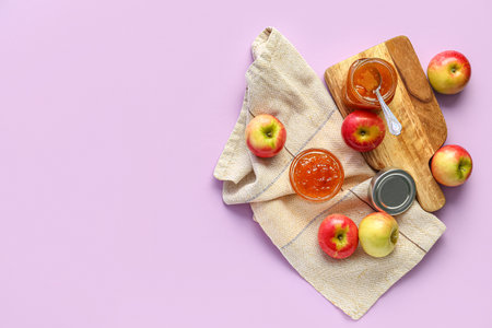 Wooden board with jar and glass bowl of sweet apple jam on purple backgroundの写真素材