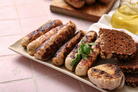 Plate of tasty grilled sausages and bread on pink tile backgroundの写真素材