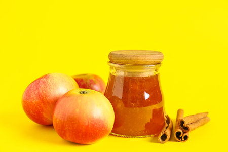 Jar of sweet apple jam with cinnamon on yellow backgroundの写真素材