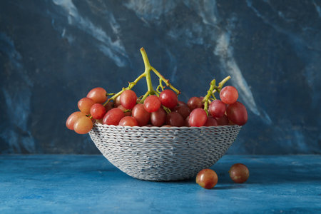 Wicker bowl with tasty ripe grapes on blue background