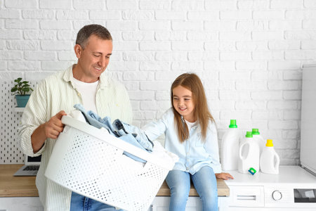 Mature man with laundry basket and his little granddaughter at homeの写真素材